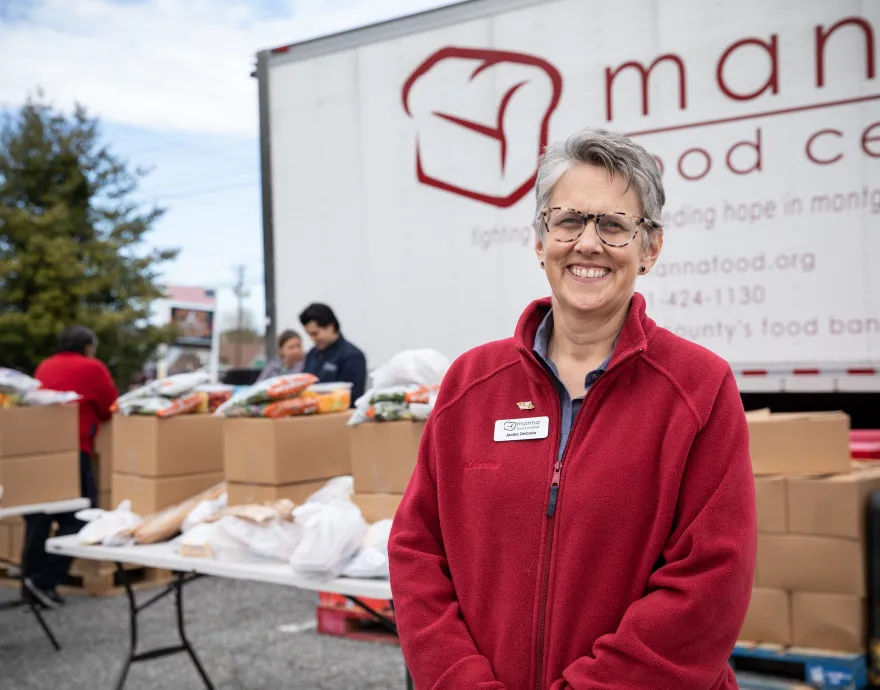 Manna Food Center's Jackie DeCarlo smiles in front of table full of food bags.