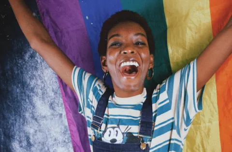 Young person holding rainbow flag and smiling