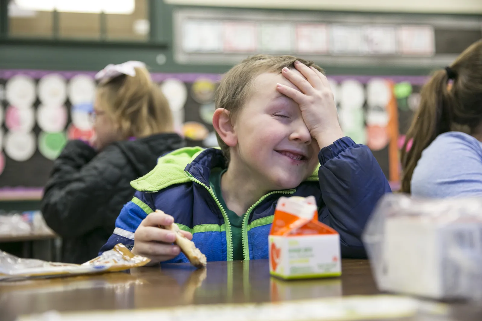 boy with hand on forehead eating breakfast in classroom