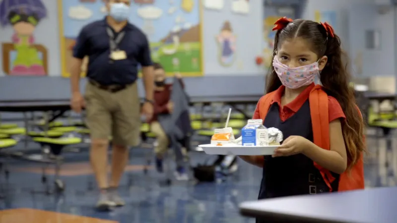 Little girl with mask holding food tray