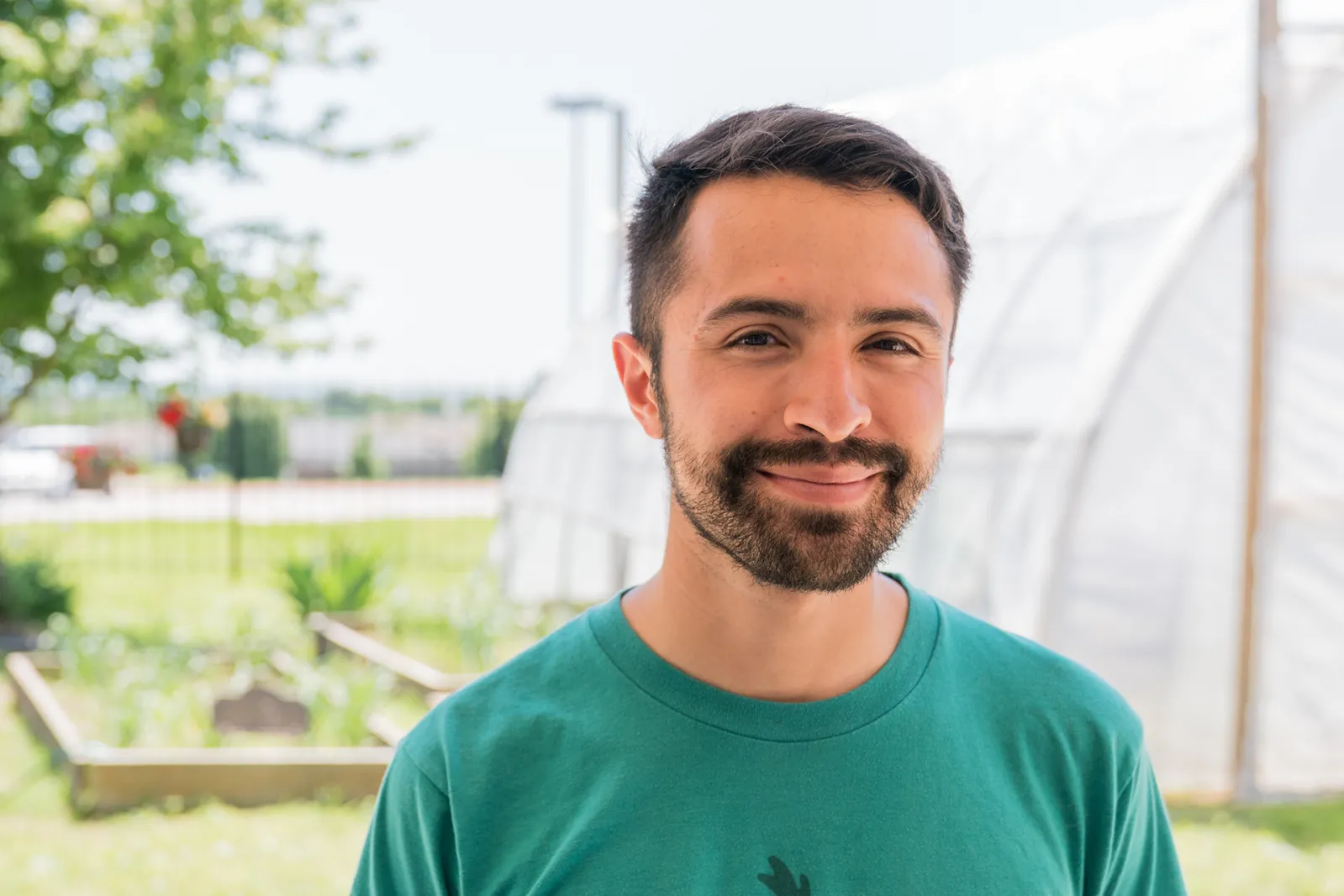 Handsome Hispanic man with beard and short hair, with greenhouse in background