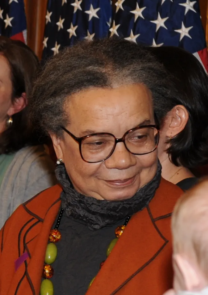 Older black woman with glasses wearing orange jacket