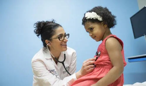 Female doctor with statoscope listening to the heart of girl wearing pink