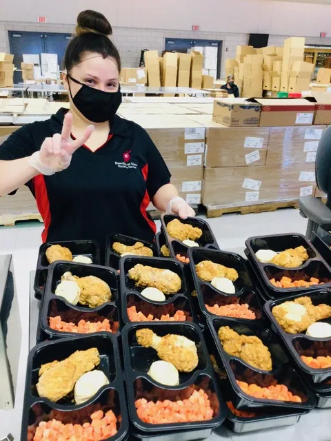 Woman wearing mask in front of trays of food