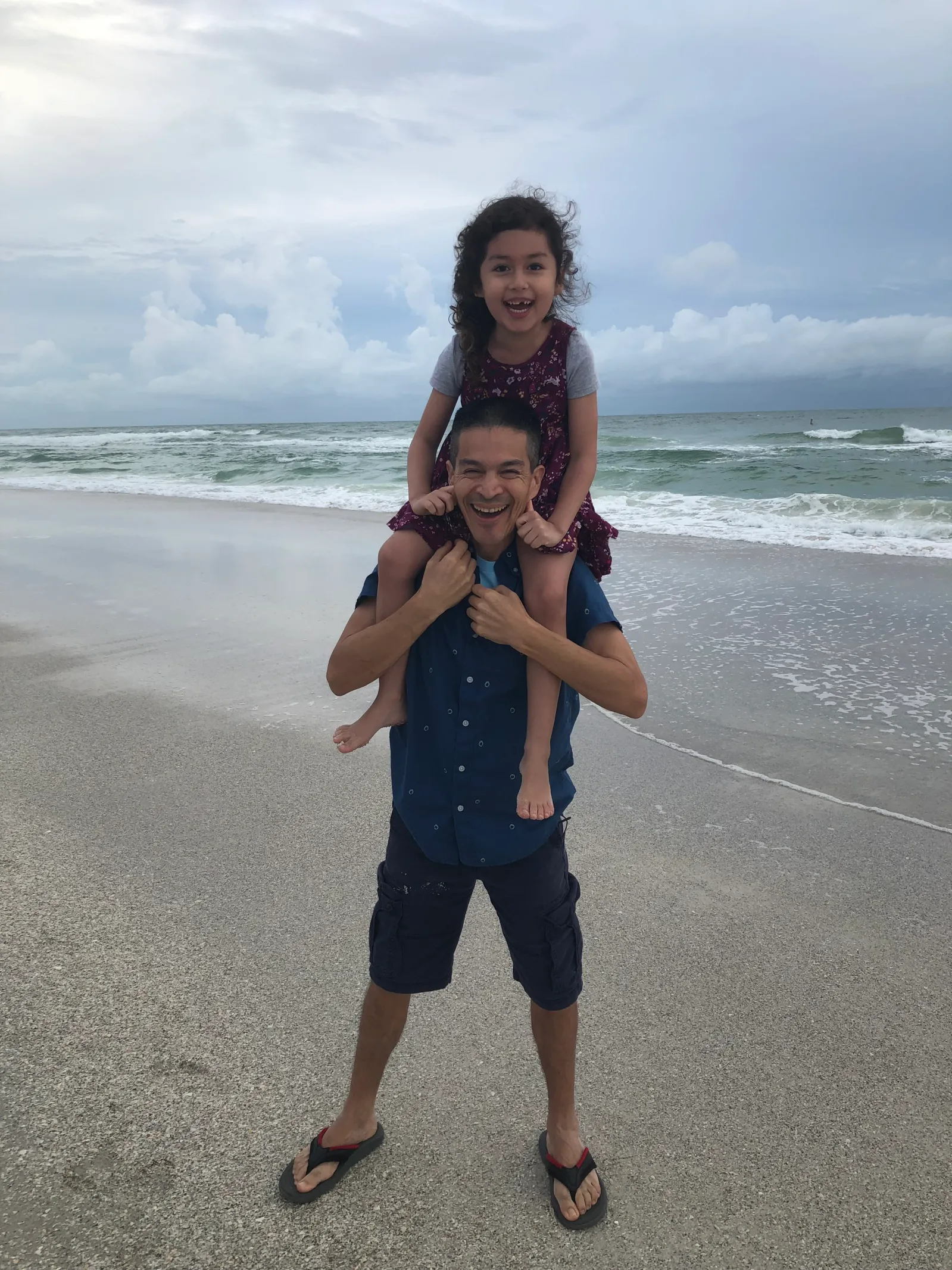 Man on beach with daughter on shoulders