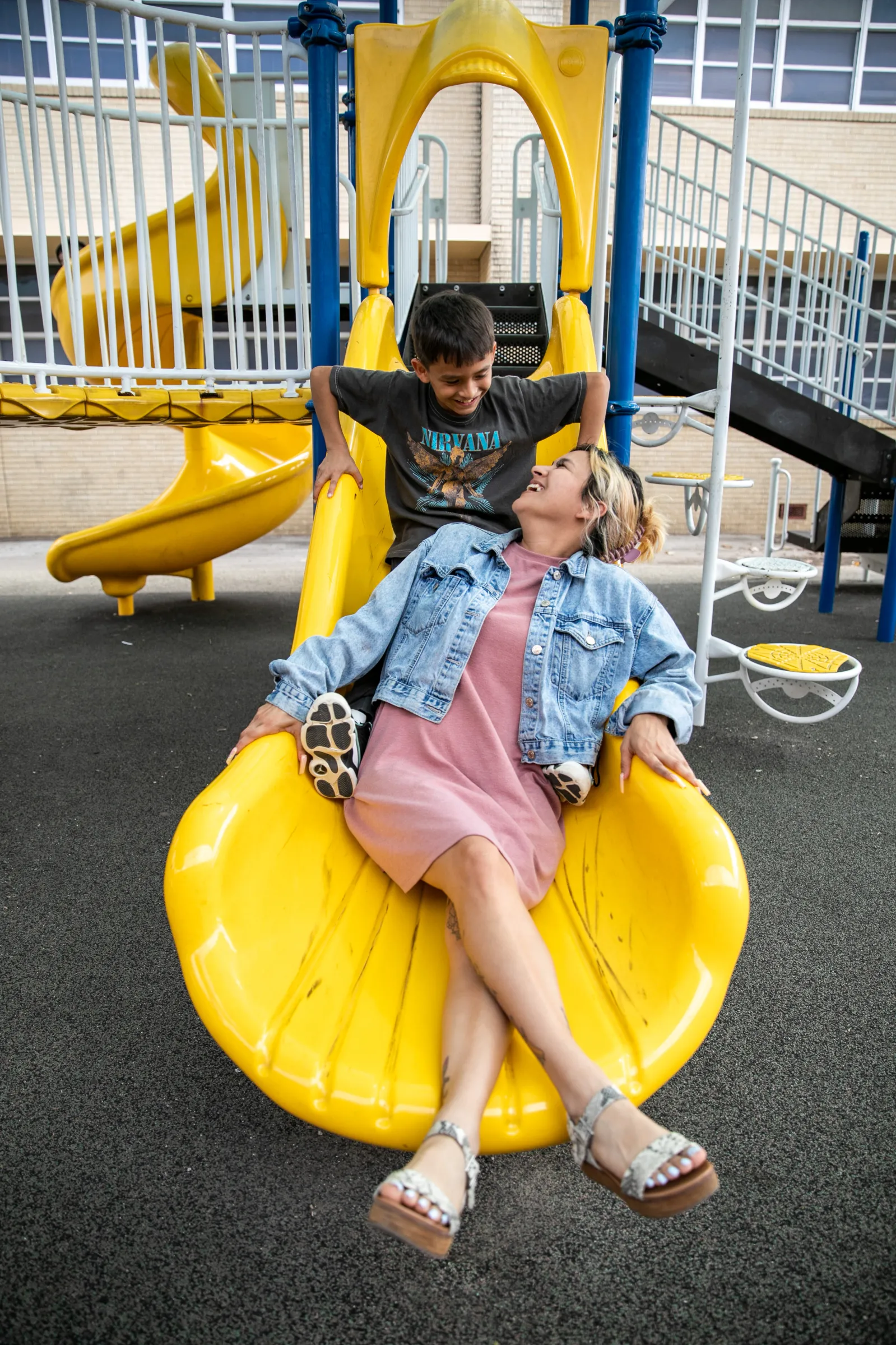 Teacher in slide of park with kid above her smiling at each other