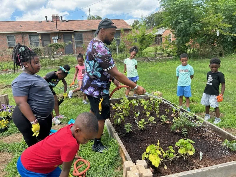 Young man watering garden surrounded by kids