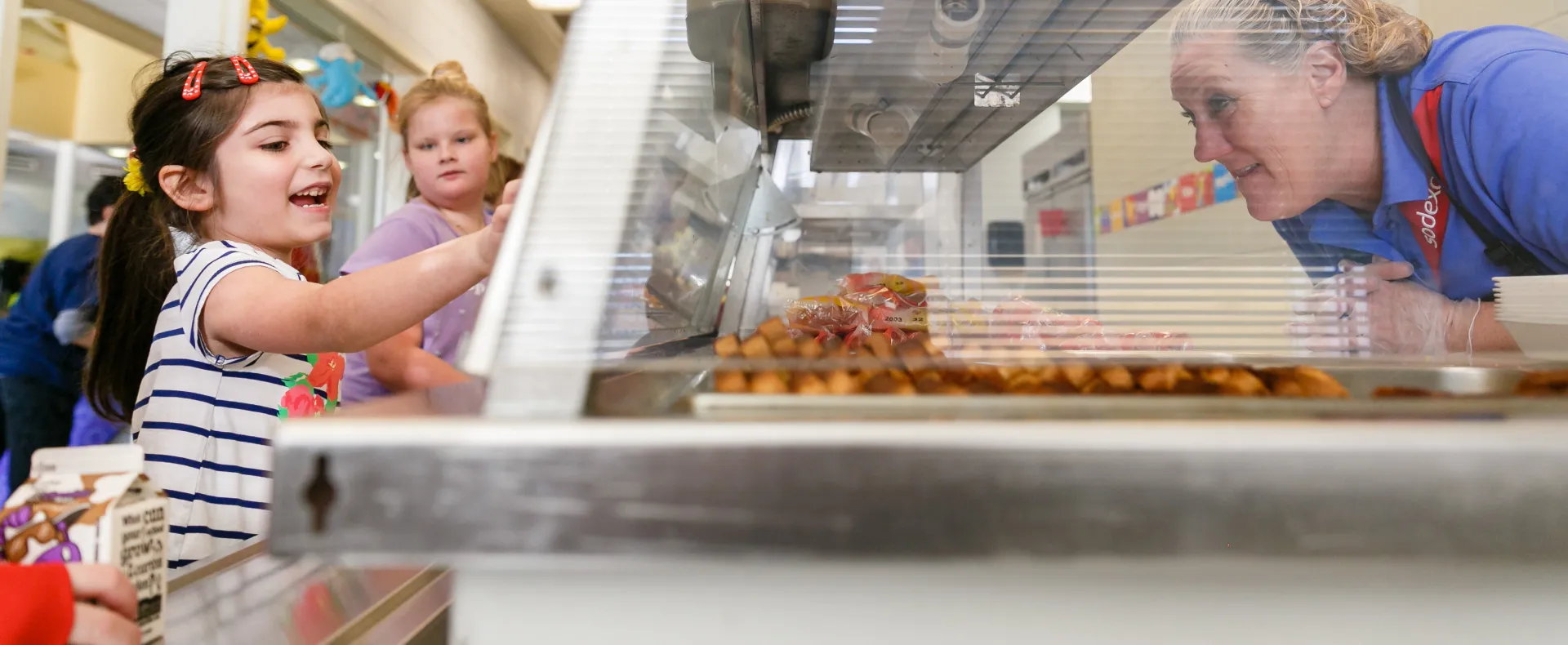 Girl pointing to food in cafeteria line for lunch lady