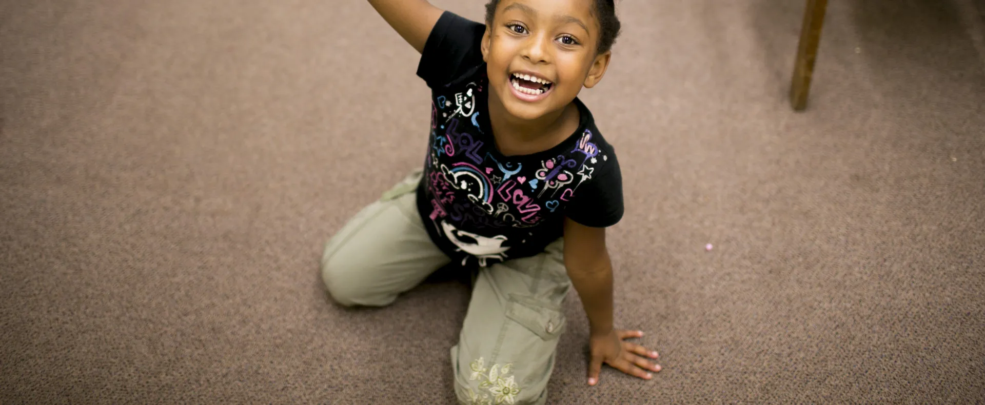 Girl sitting on her knees smiling with arms spread wide.