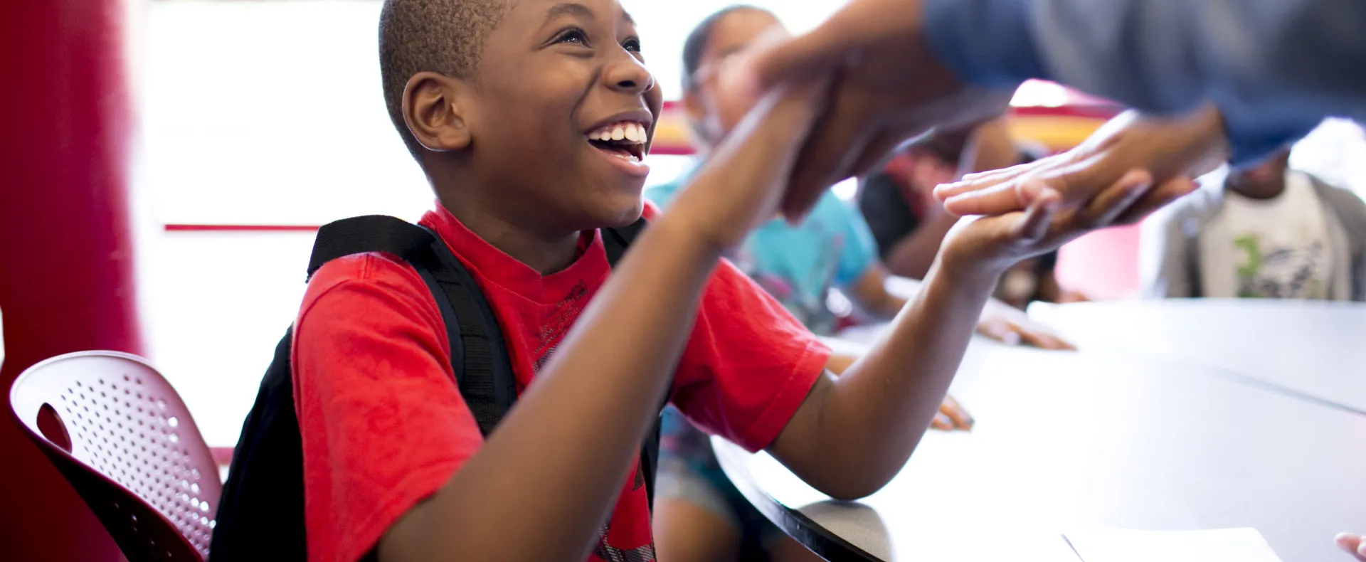 Boy sitting at a table smiling and holding hands with someone out of view