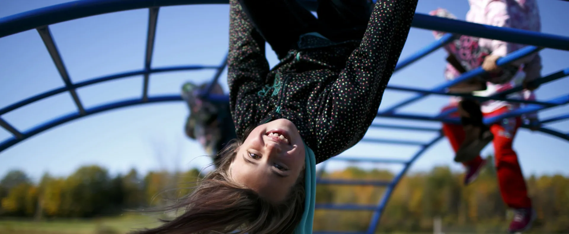 Girl hanging upside down from monkey bars