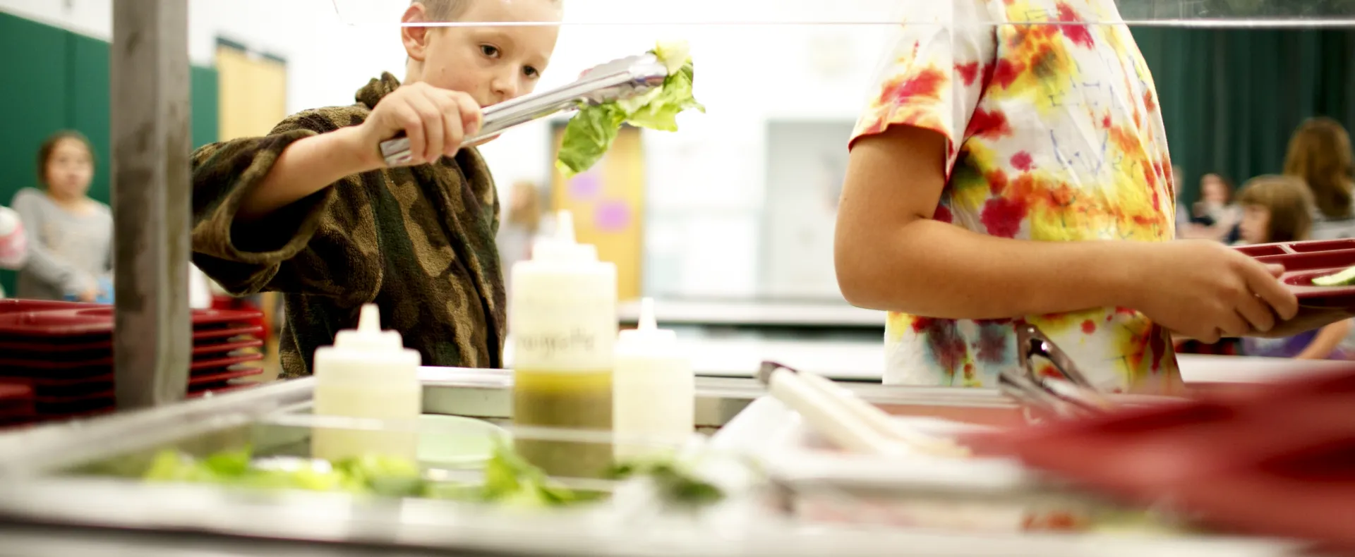 Boy holding tongs with lettuce in cafeteria line