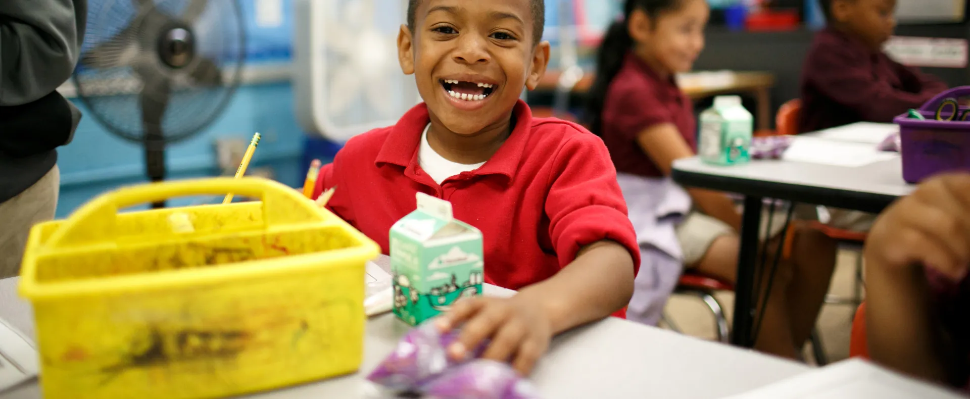Boy smiling and eating breakfast at his classroom desk