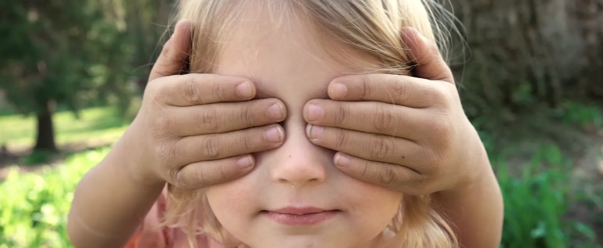 A boy holds his hands over his sister's eyes.