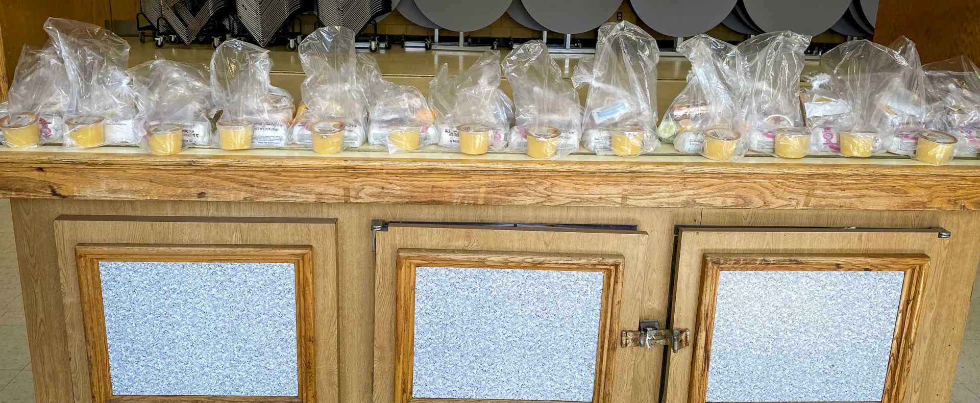 Bags of food rest atop a buffet stand, ready for families to pick up.