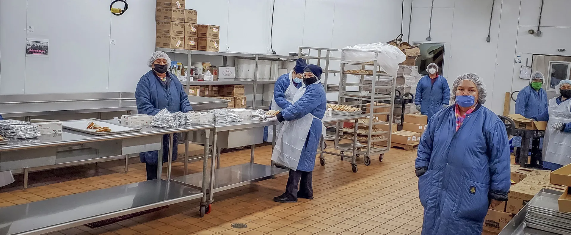 Cafeteria staff in a Laredo school kitchen prep meals while wearing masks, gloves, hairnets and aprons.