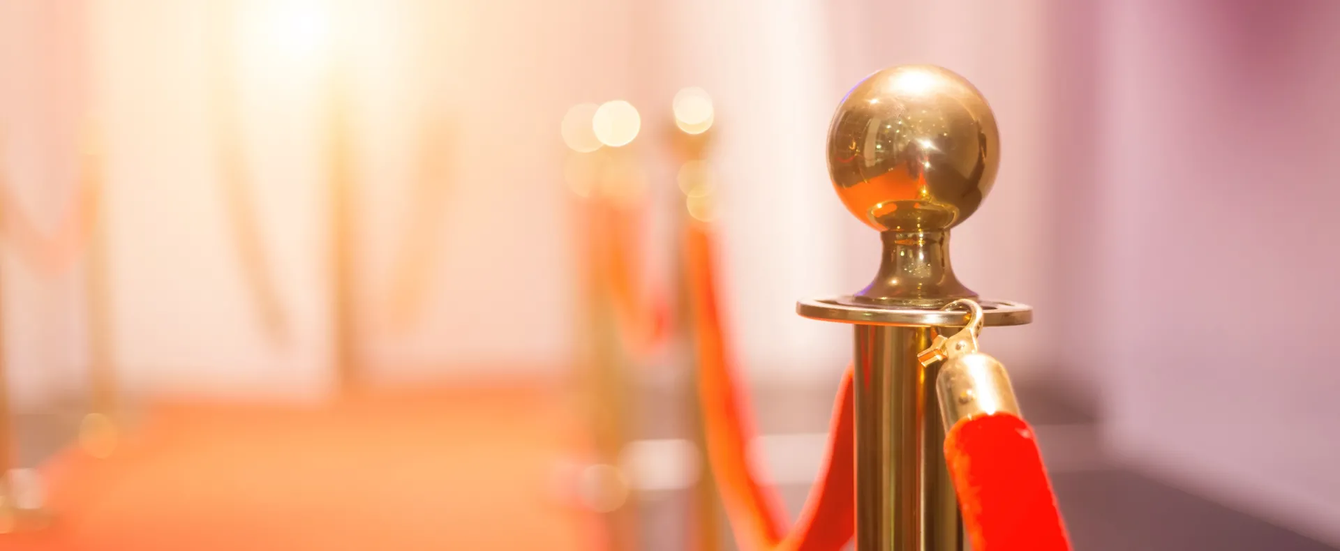 A red, velvet stanchion sits beside a red carpet.