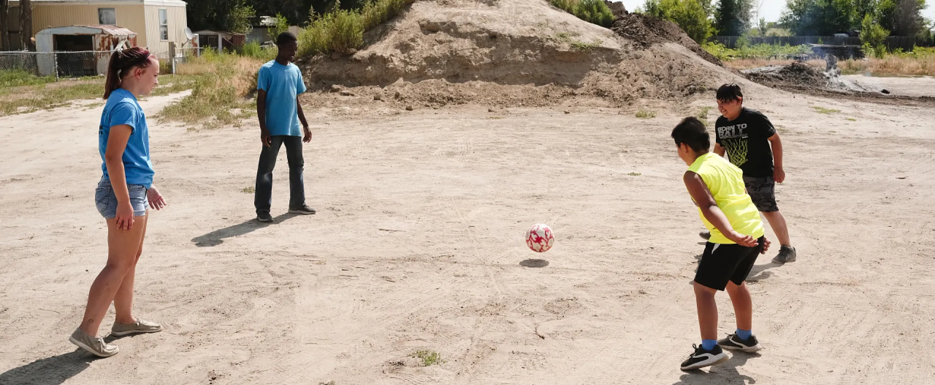 Volunteers and kids playing soccer on a barren field