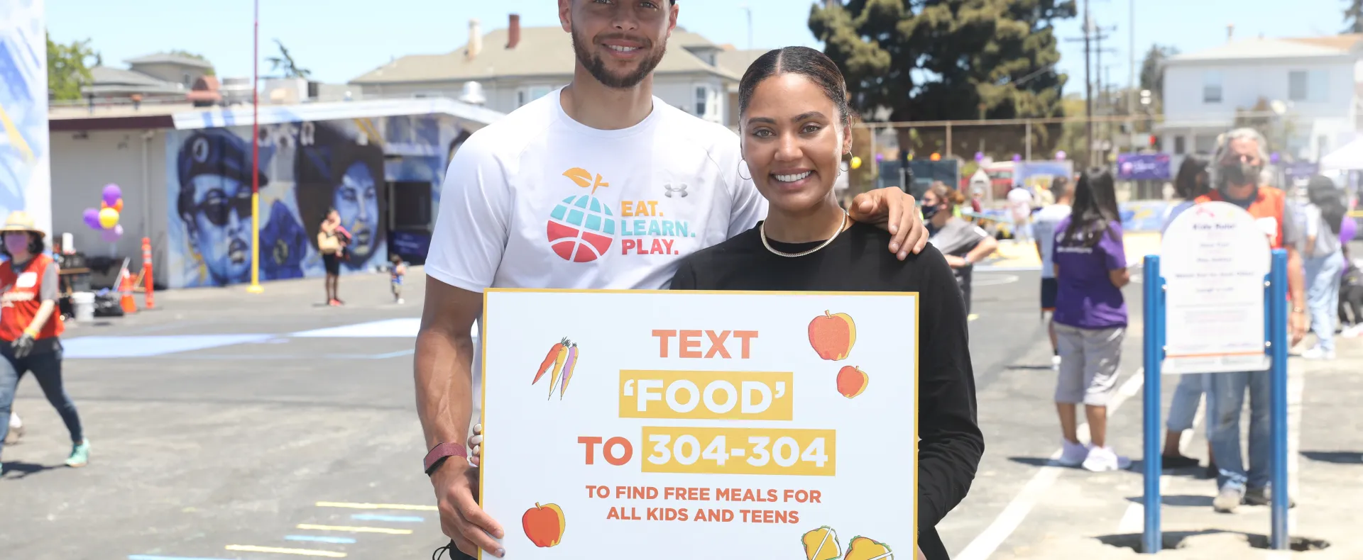 Ayesha and Stephen Curry hold a sign promoting our free meals texting service.