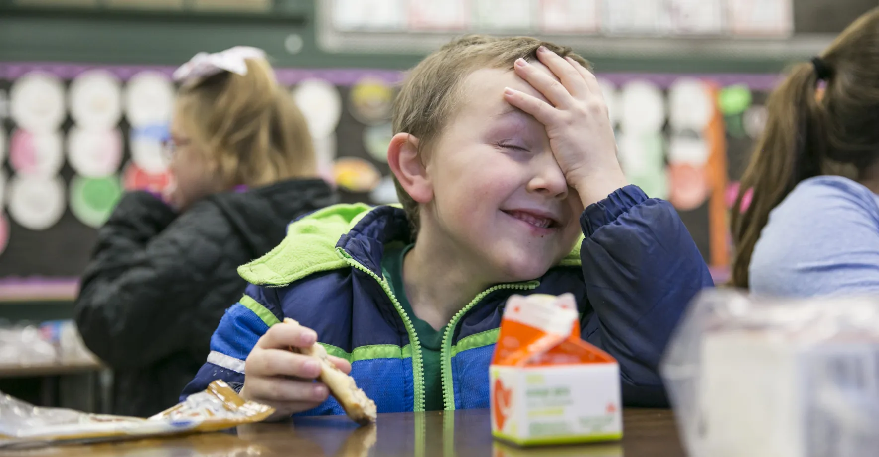 boy with hand on forehead eating breakfast in classroom