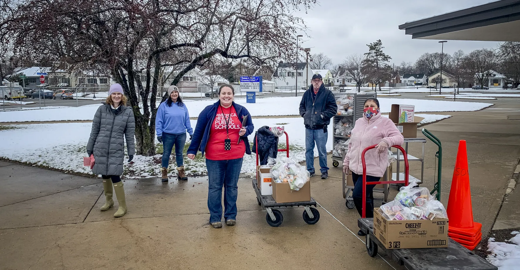 Food service staff pose outside in the snow, ready with carts of food to feed kids.