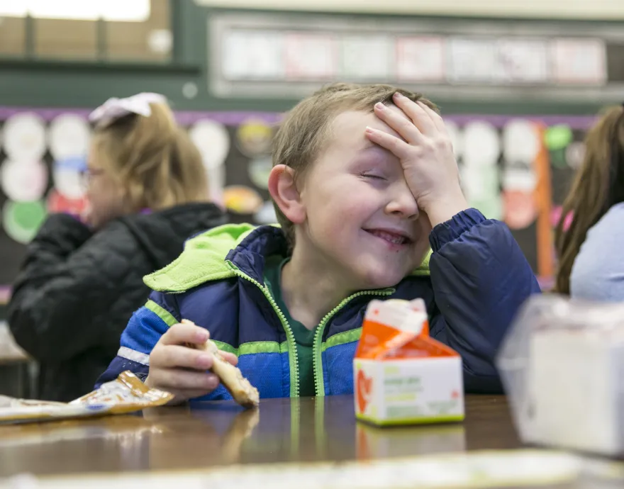 boy with hand on forehead eating breakfast in classroom