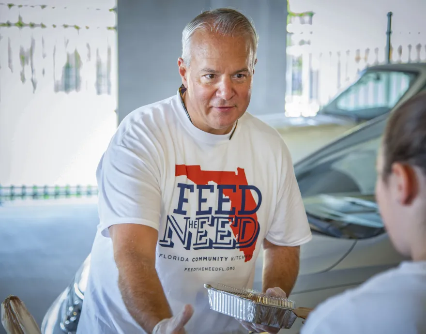 John Rivers serves meals while wearing a Feed the Need t-shirt and gloves.