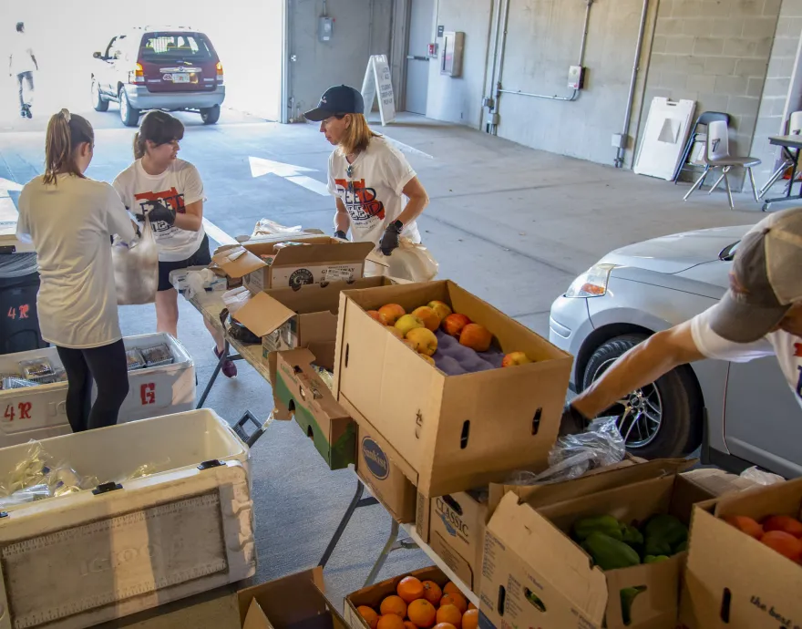 Workers pack produce into bags for cars.