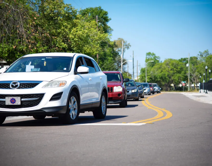 A line of cars waits for meals service on a blue sky Florida day.