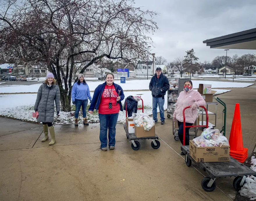 Food service staff pose outside in the snow, ready with carts of food to feed kids.