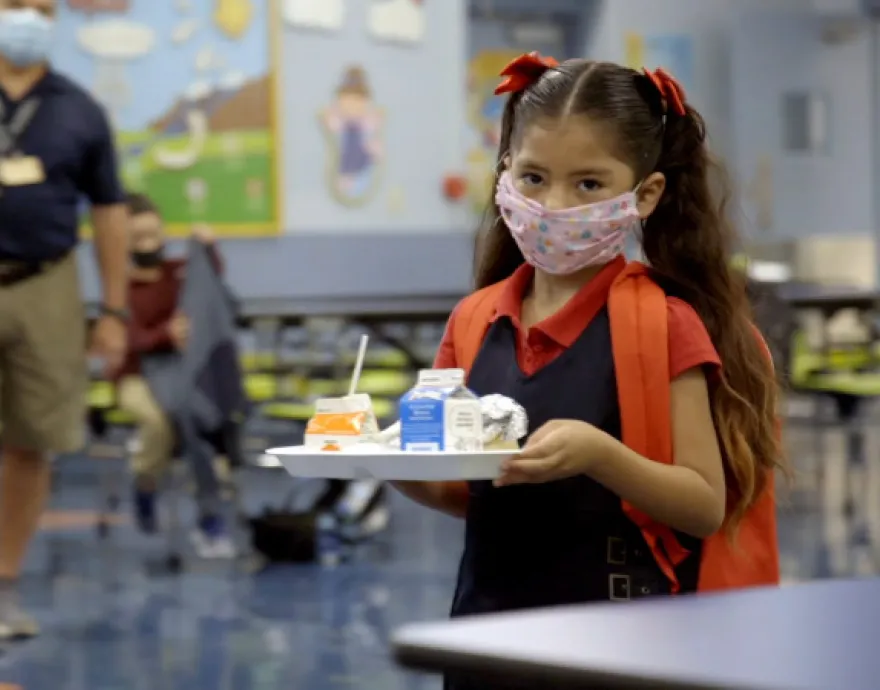 Little girl with mask holding food tray