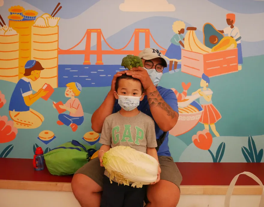 Boy holding a napa cabbage and dad putting a broccoli on his head