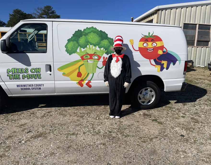 Man in costume in front of a white van decorated with an illustration of a broccoli and a tomato.