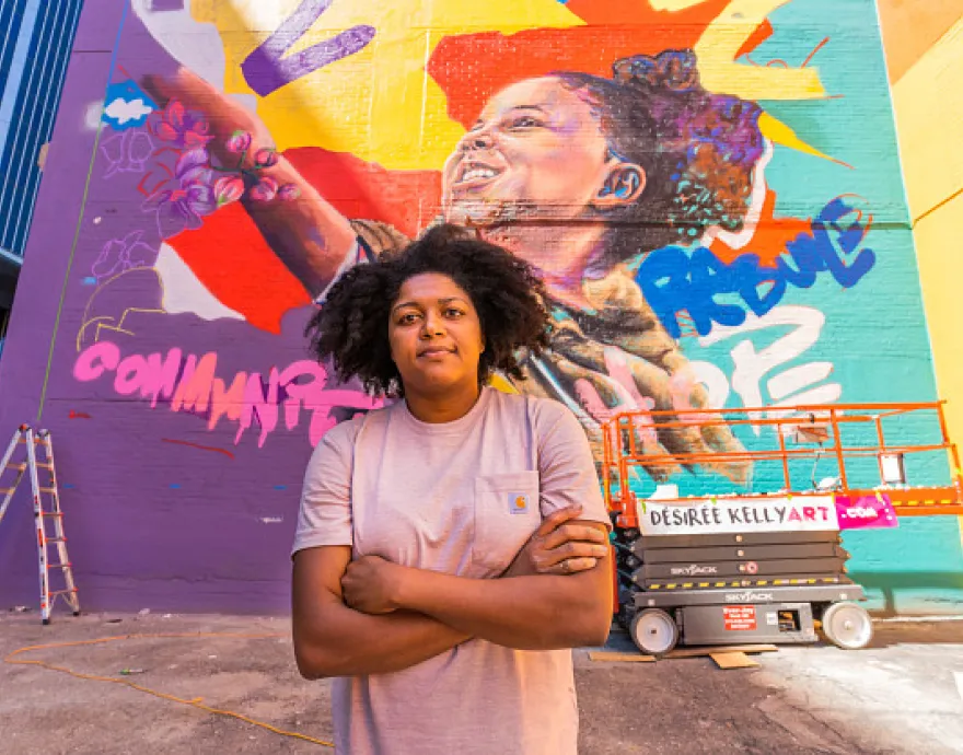 Muralist Desiree Kelly stands in front of her vibrant mural.