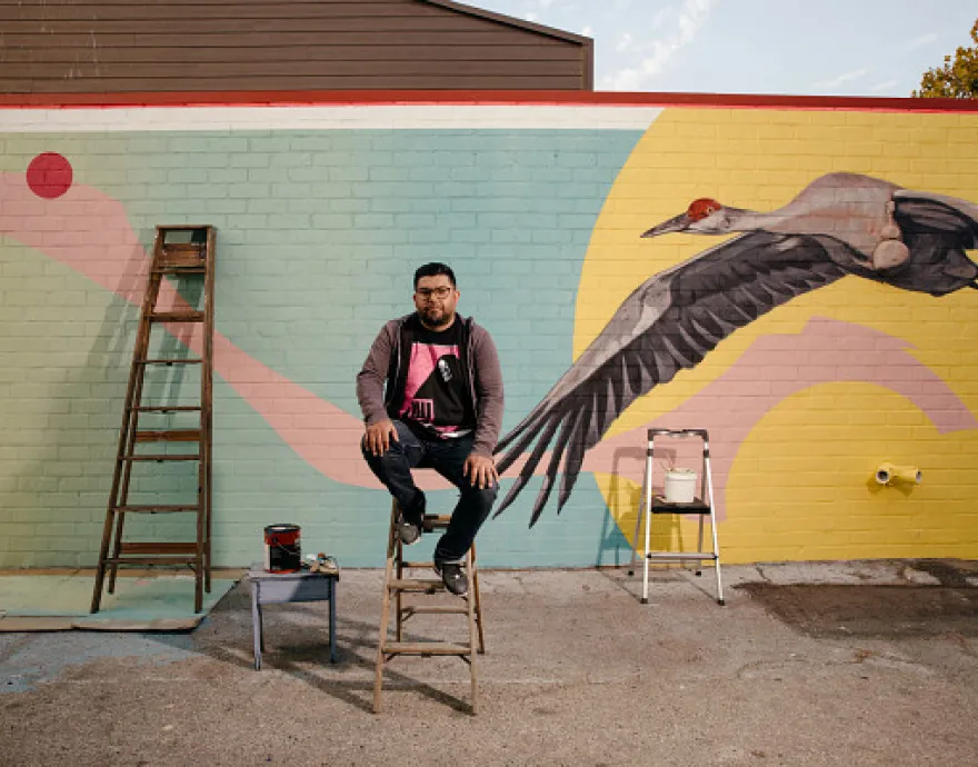 Artist Steve Martinez in front of his strikingly modern mural, with realistic images of children paired with a huge, attention-grabbing crane.