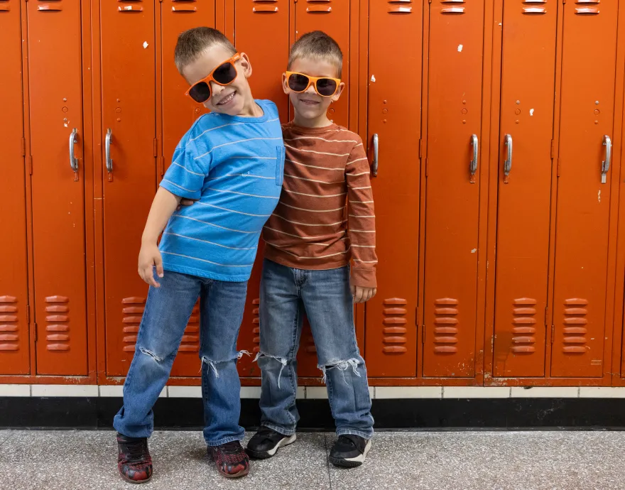 Two kids in orange No Kid Hungry sunglasses standing in front of orange lockers