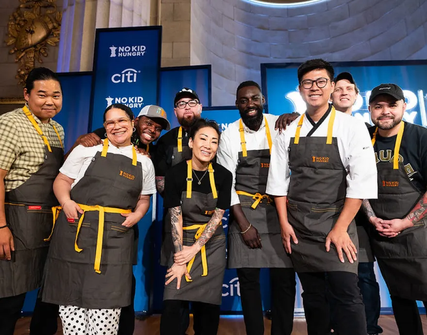 A group of celebrity chefs pose on stage at a No Kid Hungry Fundraiser