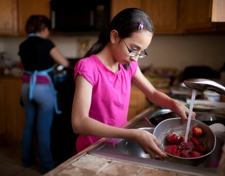Girl washing strawberries in kitchen at home