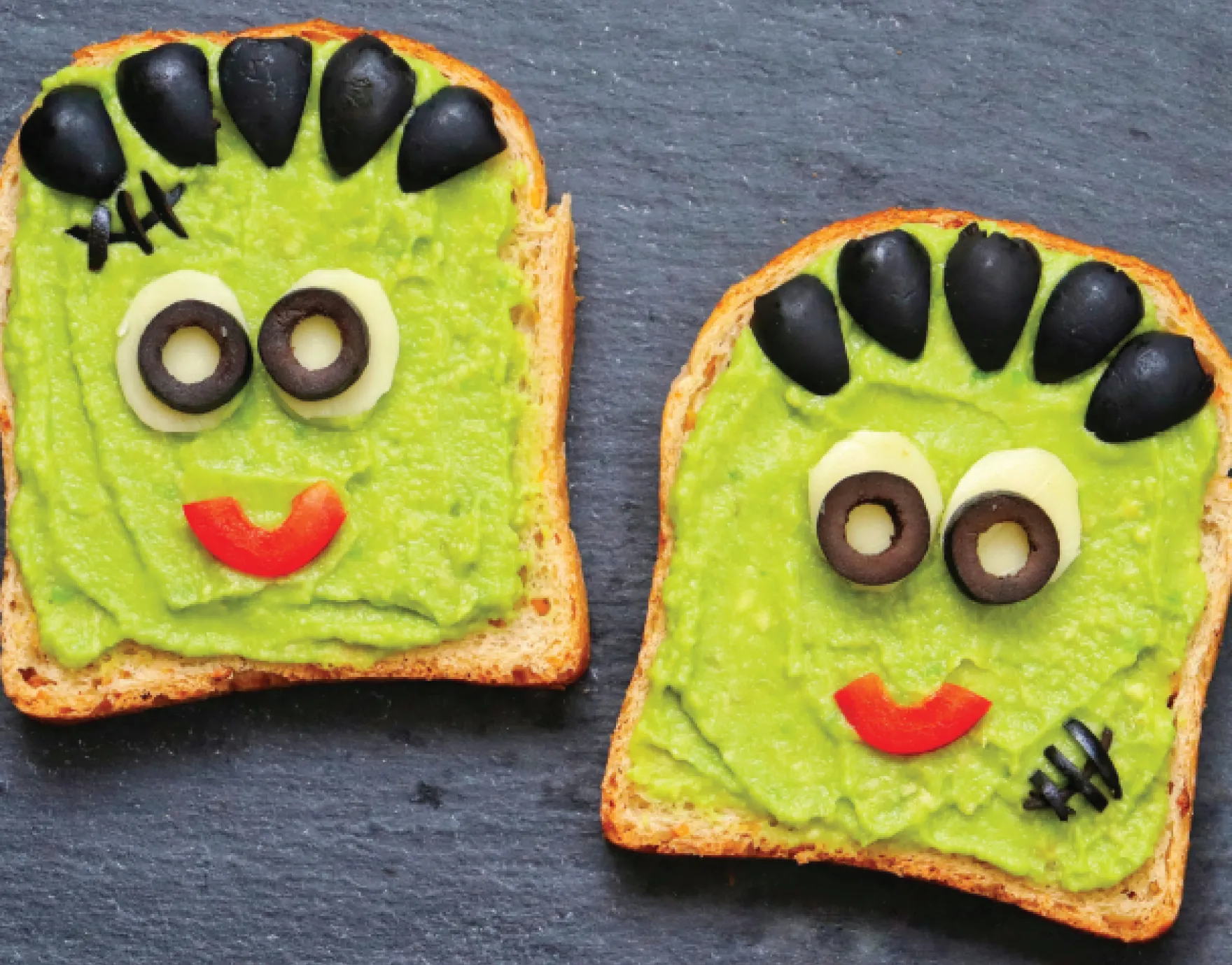 Toast decorated with avocado, olives, cheese, and red peppers to look like a monster