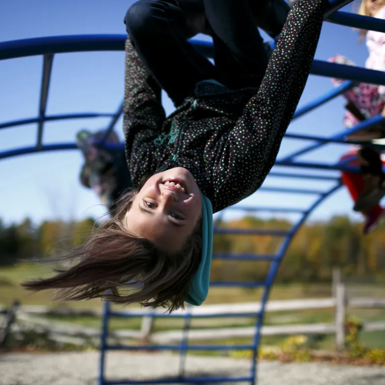 Girl hanging upside down from monkey bars