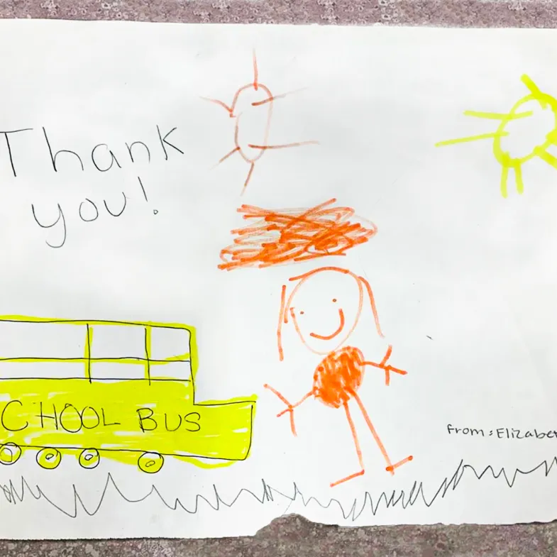 A child's drawing shows a girl waiting to receive meals from the school bus, with the words thank you written above.