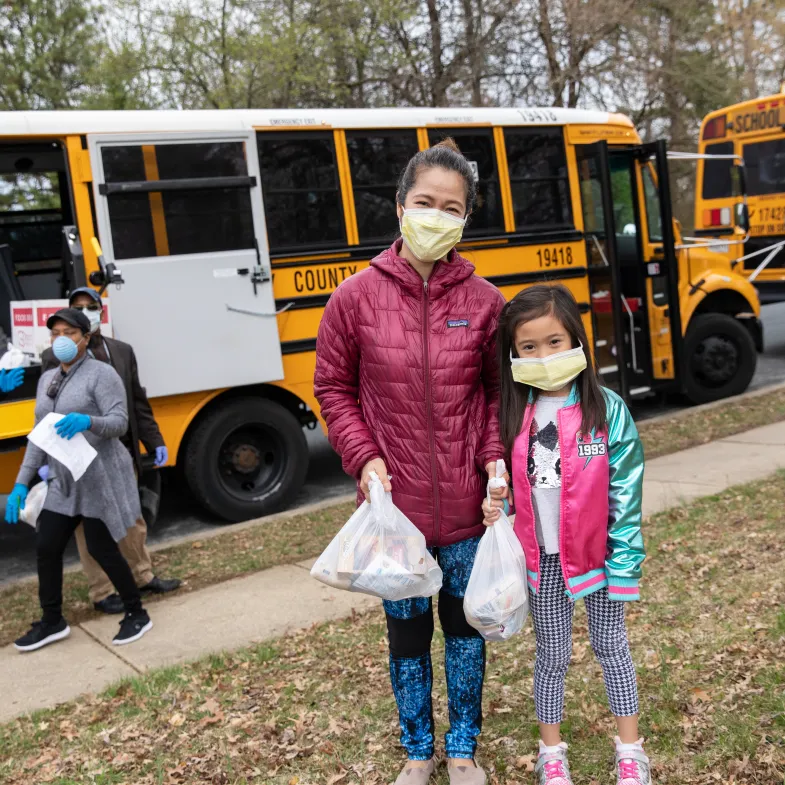 A mother and daughter pick up food at a free meals site.