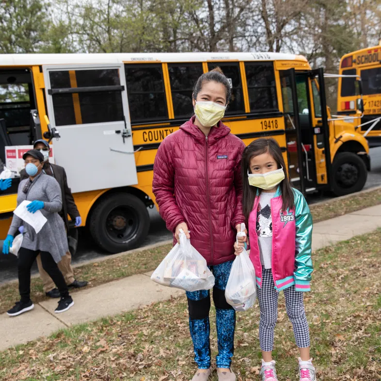 A mother and daughter wear face masks and carry their meals away from the school bus.