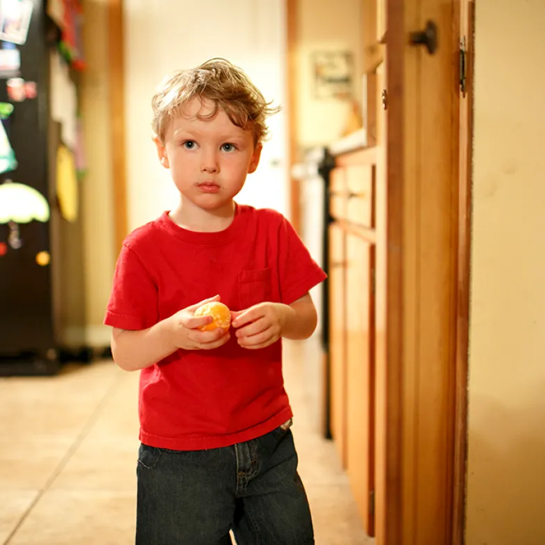 A little boy with a sad look on his face stands in his kitchen