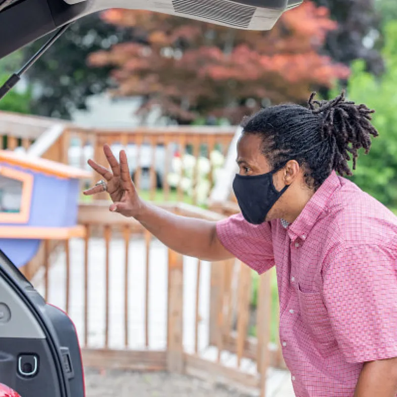 Man dropping food on a trunk. He has long hair and is wearing a mask.