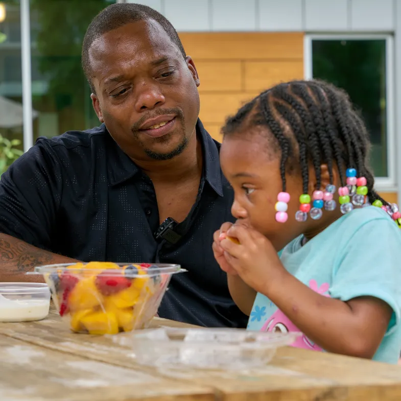 Father looking at her daughter eating a bowl of fruit
