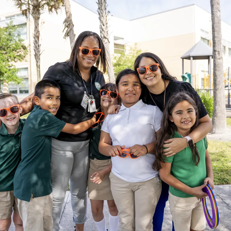 5 elementary school students (2 boys on the left and 3 girls on the right) standing with their female teachers outside Gove Elementary School in Florida.
