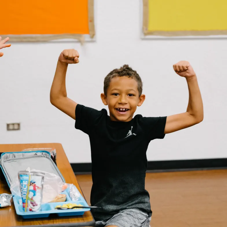 Child in classroom with arms raised