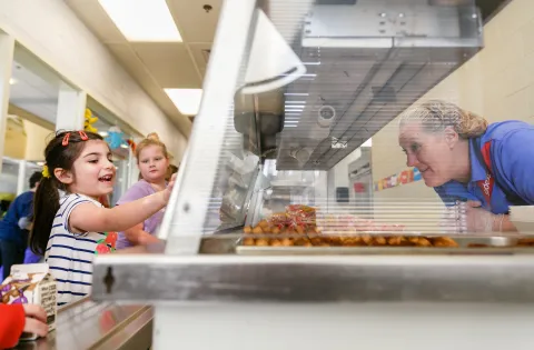 Girl pointing to food in cafeteria line for lunch lady