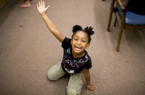 Girl sitting on her knees smiling with arms spread wide.